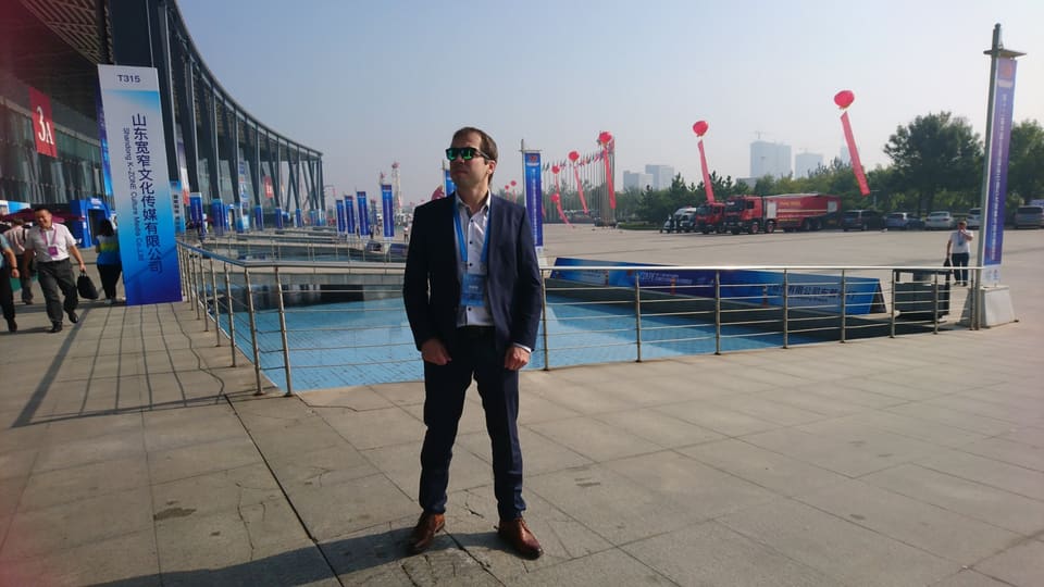 A man in a dark suit with a visitor badge outside the exhibition centre.